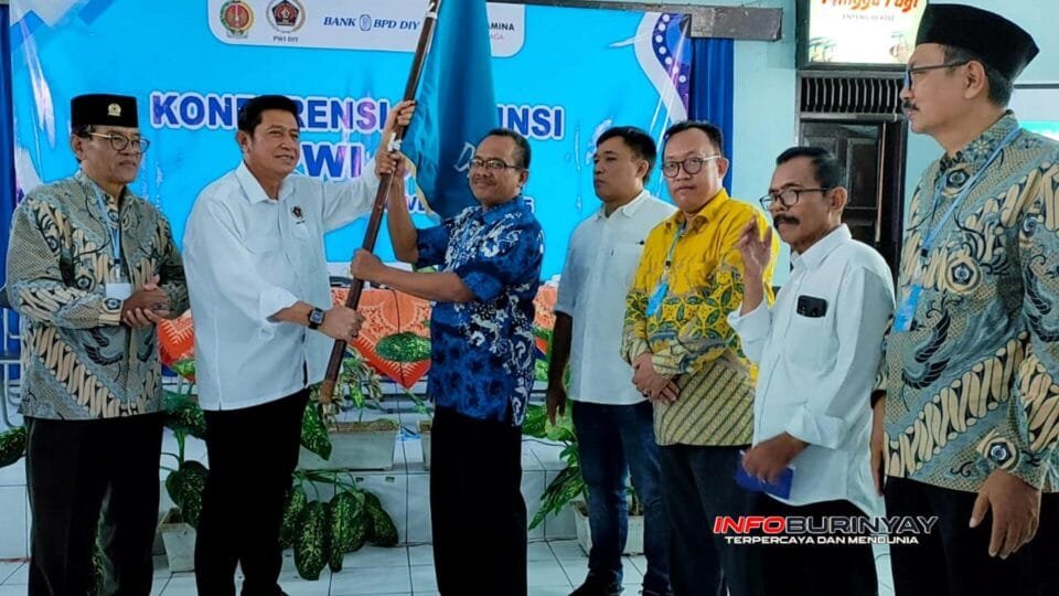 Serah terima panji organisasi dalam Konferensi Provinsi PWI DIY 2025, diikuti jajaran pengurus dan peserta konferensi.